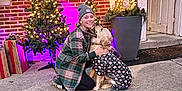 Marley Mae joined the competition — help win amazing prizes! woman, dog, golden_retriever, plaid_jacket, beanie, festive_outfit, christmas_tree, lights, brick_wall, presents, outdoor, holiday, decorations, smiling, pet, hugging, concrete, door, potted_plant, winter