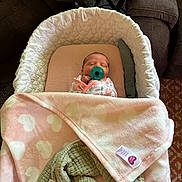 Aylin is registered to the contest to win money with this photo: baby, newborn, pacifier, bassinet, blanket, swaddle, infant, sleeping, cozy, pink, white, green, heart_pattern, couch, table, indoor, resting, cute, child, soft