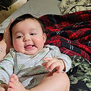 Emilio joined the competition — help win amazing prizes! baby, child, infant, smiling, happy, onesie, star_wars, foot, hand, bed, blanket, plaid, patterned_sheet, person, indoors, cozy, cute, portrait, skin, face