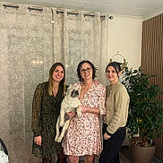 Rio a rejoint le concours — aidez-le/la à gagner de superbes lots ! black_pants, cardigan, casual_clothing, curtains, dog, floor, friendship, glasses, group, happy, home_decor, indoor, light, patterned_dress, pet, plant, room, smile, standing, woman