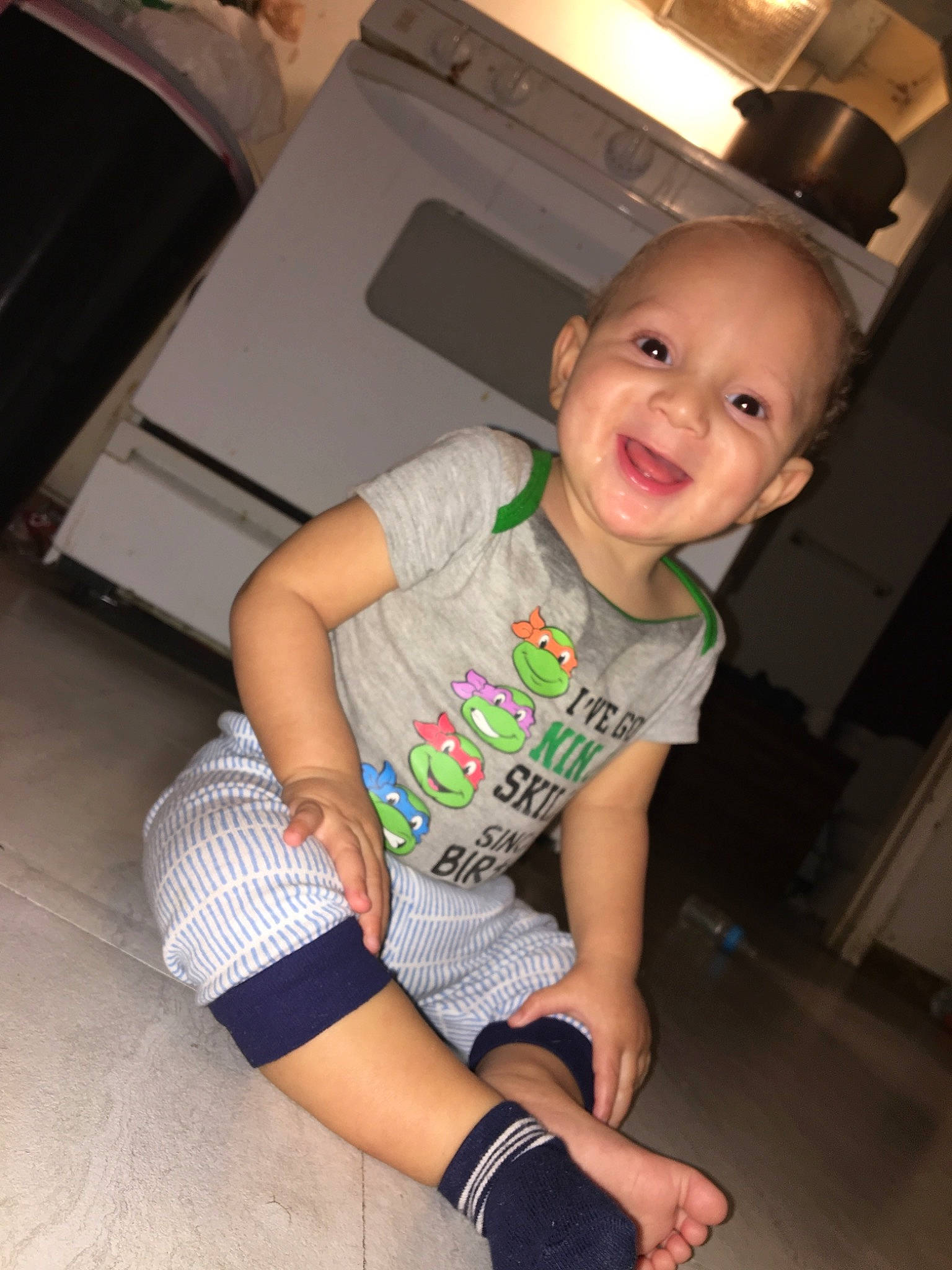 Zahkari is registered to the contest to win money with this photo: arm, baby, cheek, child, fun, joy, leg, person, play, shoe, sitting, skin, smile, t_shirt, toddler