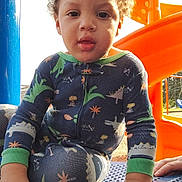 Za'Marion is registered to the contest to win money with this photo: child, toddler, playground, slide, orange, blue, pajamas, dinosaur_pattern, curly_hair, hand, face, outdoor, sunlight, daylight, play, clothing, person, young_child, expression, park