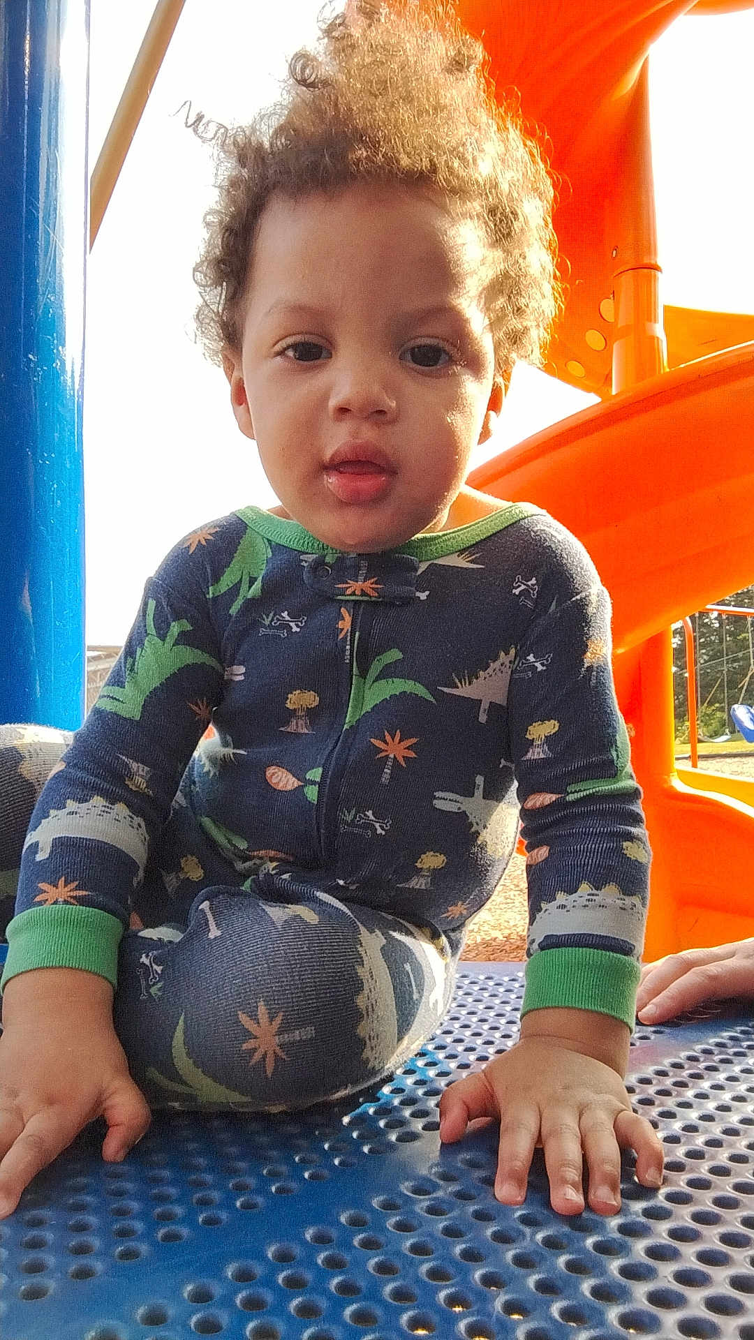 Za'Marion is registered to the contest to win money with this photo: child, toddler, playground, slide, orange, blue, pajamas, dinosaur_pattern, curly_hair, hand, face, outdoor, sunlight, daylight, play, clothing, person, young_child, expression, park