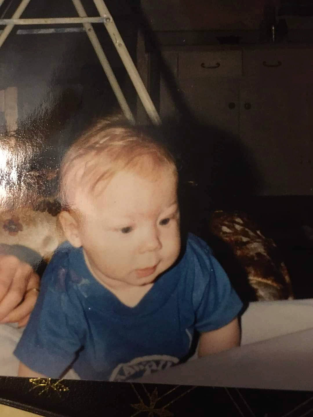 Killian is registered to the contest to win money with this photo: arm, baby, cheek, child, comfort, darkness, finger, flash_photography, fun, hand, happy, iris, mouth, person, room, sitting, t_shirt, tints_and_shades, toddler, wood