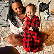 Christopher joined the competition — help win amazing prizes! baby, woman, indoor, carpet, red_clothing, plaid_pattern, smiling, sitting, supporting, furniture, television, cabinet, floor, person, home, light, face, child, holding, curious