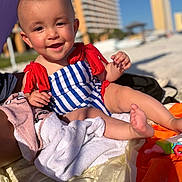 Gradie is registered to the contest to win money with this photo: baby, beach, building, child, colorful, face, foot, hand, happy, outdoor, person, relaxing, sand, smiling, summer, sunlight, swimsuit, towel, toy, vacation