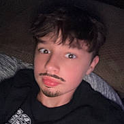 Jayce is registered to the contest to win money with this photo: child, boy, selfie, indoors, couch, black_sweatshirt, text_on_clothing, facial_hair_drawn, mustache, goatee, casual, young, portrait, face, hair, relaxed, seated, funny, expression, home
