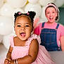 accessories, baby, balloons, bracelets, celebration, child, clothing, cute, earrings, fun, hair_buns, happy, indoor, joy, person, pink_dress, portrait, smiling, toddler, yellow_background
