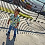 Jace joined the competition — help win amazing prizes! child, boy, standing, shadow, outdoor, sunny, pavement, fence, metal_fence, casual_clothing, jeans, shirt, smiling, candy, footwear, crocs, daylight, urban, parking_lot, playful