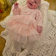 Rosie joined the competition — help win amazing prizes! baby, infant, pink_dress, headband, smiling, crocheted_blanket, white_shoes, tights, indoor, floor, wooden_floor, portrait, cute, happy, child, person, soft_lighting, cozy, celebration, holiday_decor