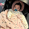 baby, pacifier, blanket, car_seat, plush_toy, hooded_jacket, pink, heart_pattern, infant, child, cute, warm_clothing, indoor, seated, portrait, face, expression, comfort, soft_toy, cozy