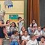 blue_jeans, casual_clothing, children, classroom, cloud, decoration, gathering, group, indoor, kids, kids_playing, mixed_ethnicity, painting, raindrops, seated, steps, striped_shirt, teacher, white_shirt, woman
