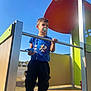 black_pants, blue_sky, boy, casual_clothing, child, daytime, holding, metal_rail, outdoor, pacifier, play_equipment, playground, shade, sneakers, sonic_the_hedgehog, standing, sunlight, toy, tshirt, young