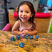 Claire is registered to the contest to win money with this photo: child, girl, smiling, happy, toy, figurine, stitch, tabletop, granite, kitchen, indoor, play, cute, hair, clothing, person, face, expression, colorful, background