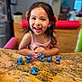 child, girl, smiling, happy, toy, figurine, stitch, tabletop, granite, kitchen, indoor, play, cute, hair, clothing, person, face, expression, colorful, background