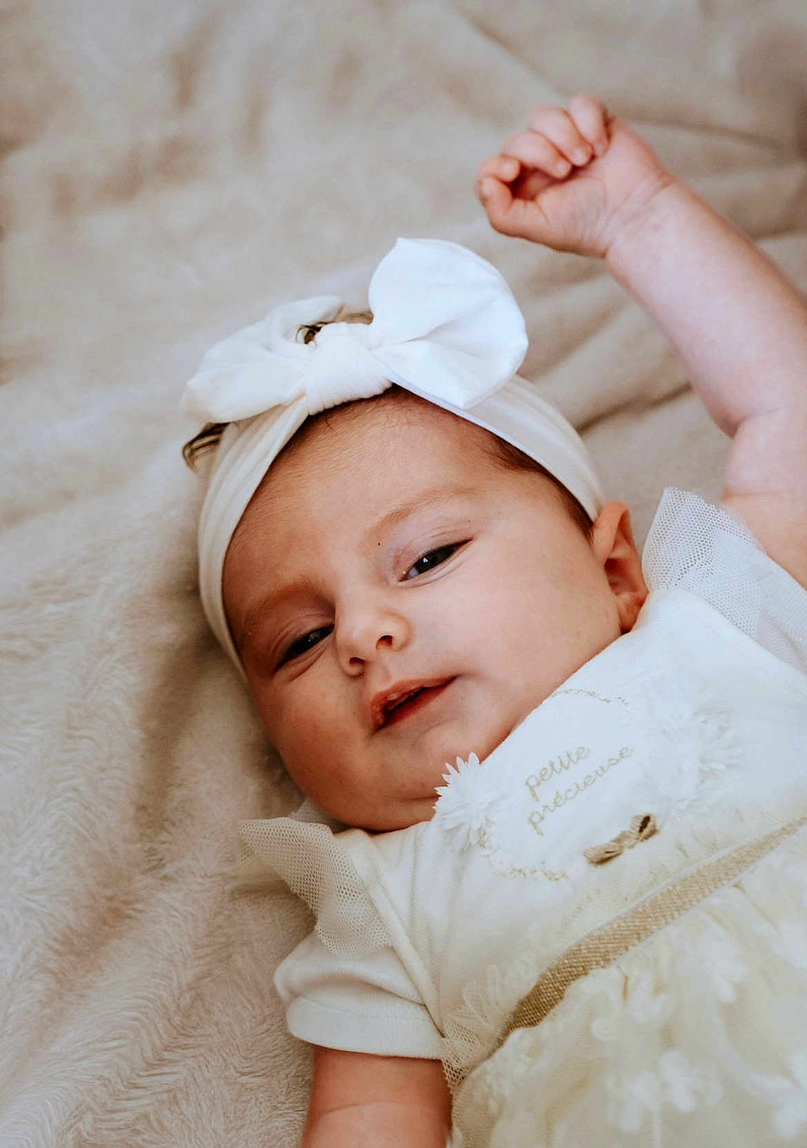 Esmée a rejoint le concours — aidez-le/la à gagner de superbes lots ! baby, infant, white_dress, headband, bow, soft_blanket, lying_down, cute, portrait, child, smiling, skin, face, arm, relaxed, indoors, young, toddler, clothing, person