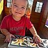 child, toddler, smiling, portrait, outdoor, playhouse, wooden_cabin, sunlight, toy, sandbox, construction, hands, red_shirt, texas_tech, table, playtime, happy, face, daylight, family_photo