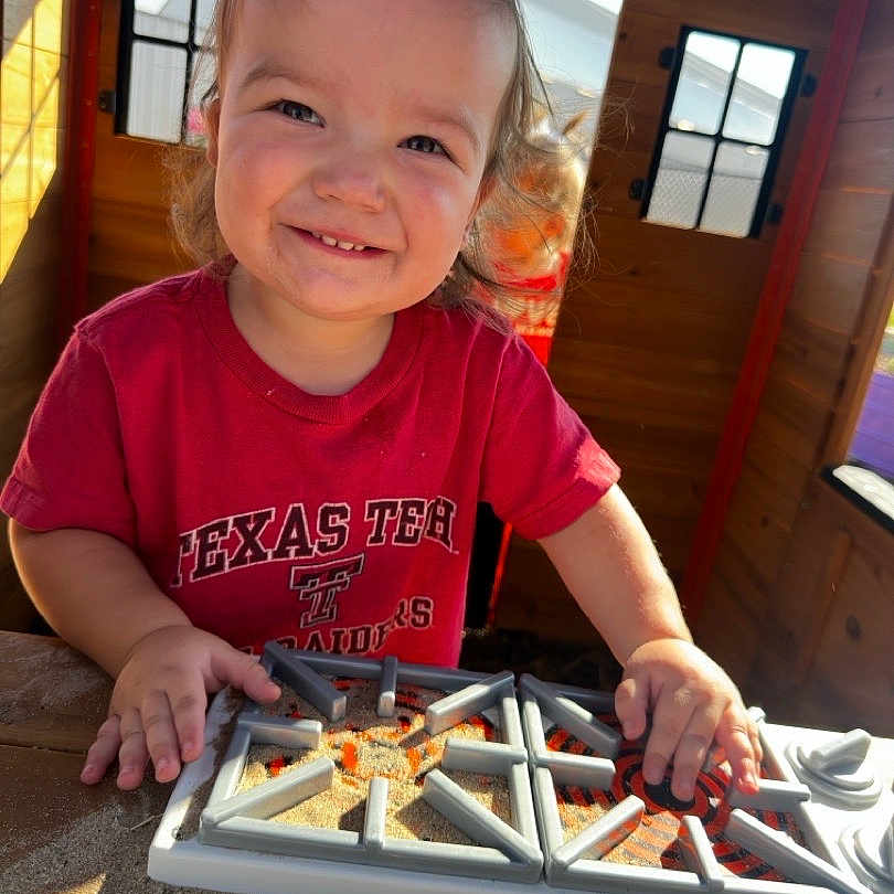 Brooks joined the competition — help win amazing prizes! child, toddler, smiling, portrait, outdoor, playhouse, wooden_cabin, sunlight, toy, sandbox, construction, hands, red_shirt, texas_tech, table, playtime, happy, face, daylight, family_photo