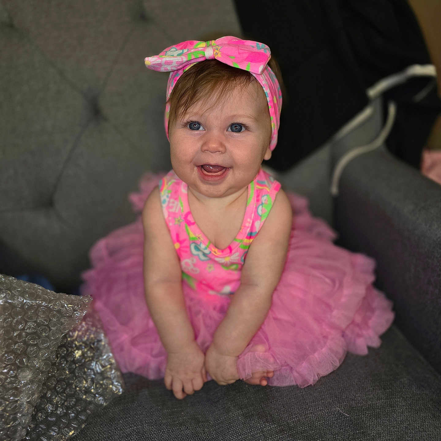 Sayler joined the competition — help win amazing prizes! baby, blue_eyes, bubble_wrap, child, clothing, cute, face, fashion, fun, gray_chair, happy, headband, indoor, infant, person, pink_tutu, portrait, sitting, smiling, toddler