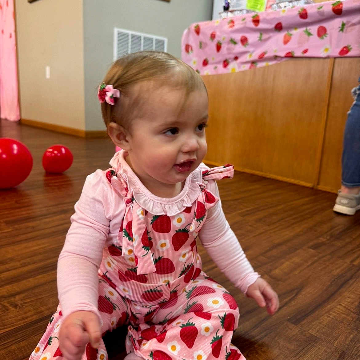 Amiyah joined the competition — help win amazing prizes! baby, balloon, cabinet, child, floor, hair_clip, home, indoor, kitchen, long_sleeve_shirt, overalls, person, pink_clothing, play, red_balloon, sitting, strawberry_pattern, tablecloth, toddler, wood_floor