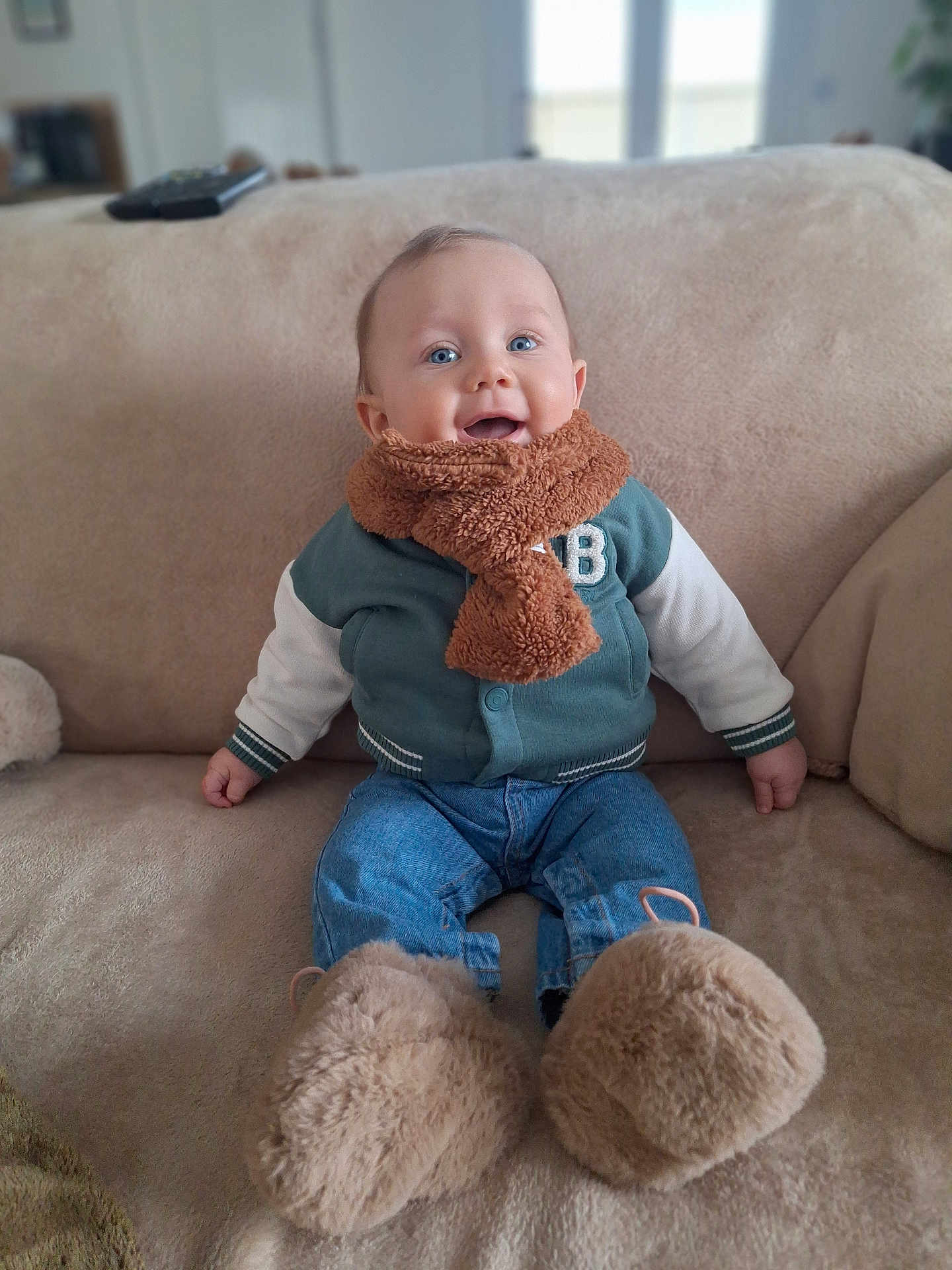 Ewen participe au concours pour gagner de l'argent avec cette photo : baby, child, smiling, scarf, jacket, blue_eyes, sitting, couch, remote_control, indoor, cozy, fluffy_slippers, jeans, happy, portrait, furniture, warm_clothing, cute, infant, home