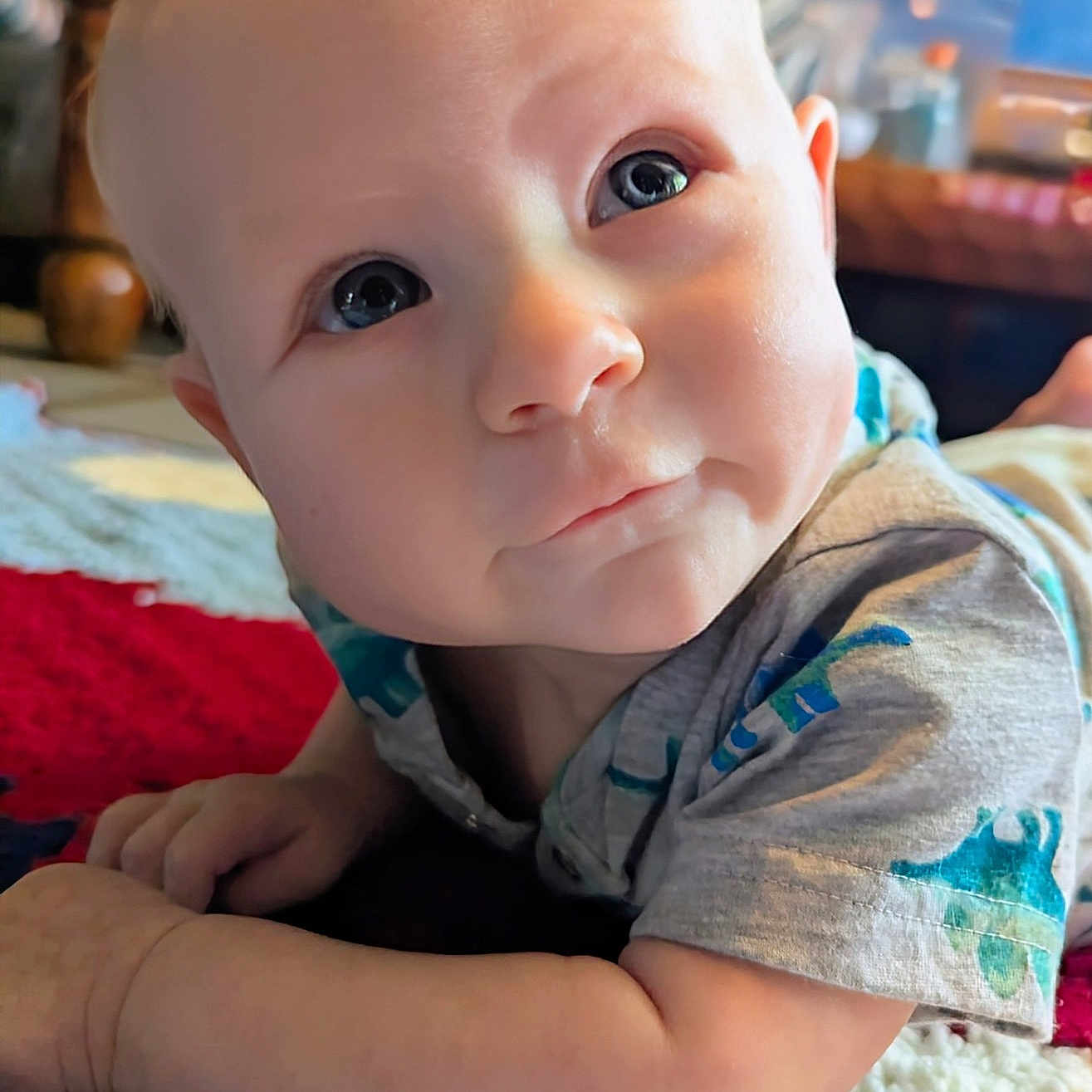 Malakai is registered to the contest to win money with this photo: baby, blanket, blue_eyes, child, closeup, clothing, curious, cute, expression, face, indoors, infant, innocence, knitted, lying_down, portrait, short_sleeve, skin, soft_light, young