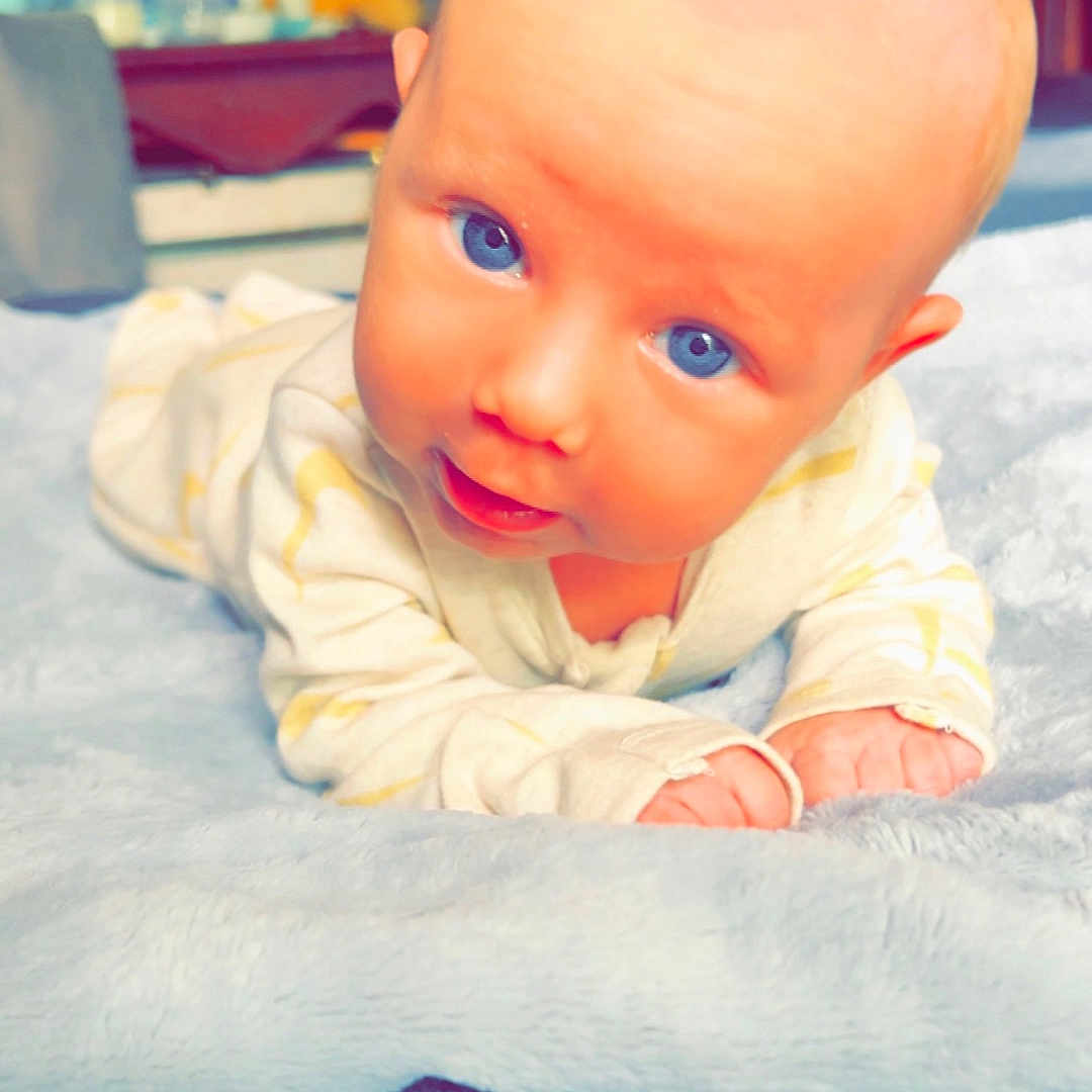 Kayden is registered to the contest to win money with this photo: baby, babycrawling, bed, bodypart, clothing, crawling, dress, face, finger, hand, happy, head, newborn, pants, person, photography, portrait, quilt, sitting, smile