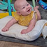 baby, infant, child, smiling, happy, portrait, tummy_time, yellow_outfit, play_mat, baby_cushion, toy, play_gym, bookshelf, indoor, home, floor, carpet, sitting, face, photography