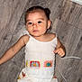 baby, casual, child, clothing, colorful, crochet, cute, earrings, expression, floor, hand, head, home, indoor, looking_at_camera, person, sleeveless, toddler, white_outfit, wooden_floor