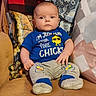 Wyatt is registered to the contest to win money with this photo: baby, infant, child, sitting, couch, blanket, pillow, blue_shirt, graphic_tshirt, chick_design, sunglasses_graphic, pants, shoes, portrait, indoors, furniture, cozy, wide_eyed, text_on_clothing, home