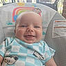 baby, infant, child, smiling, portrait, close_up, face, eyes, indoors, baby_bouncer, seat, blanket, blue_clothing, checkered_pattern, cartoon, rainbow, clouds, monkey, nursery, happy