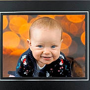 Amelia joined the competition — help win amazing prizes! baby, blue_eyes, smile, sweater, bird_pattern, floral_pattern, portrait, indoor, bokeh, orange_background, close_up, child, cute, happy, framed_photo, cozy_clothing, infant, face, head, person