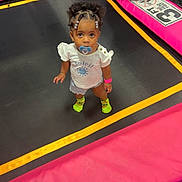 Anilah is registered to the contest to win money with this photo: toddler, child, pacifier, trampoline, pink, yellow, neon_socks, curly_hair, bracelet, white_shirt, shorts, indoor, looking_up, play_area, footwear, cute, small_child, vibrant_colors, standing, young
