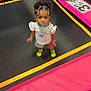toddler, child, pacifier, trampoline, pink, yellow, neon_socks, curly_hair, bracelet, white_shirt, shorts, indoor, looking_up, play_area, footwear, cute, small_child, vibrant_colors, standing, young