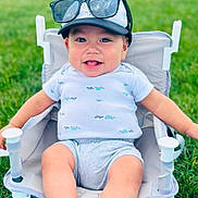Asher joined the competition — help win amazing prizes! baby, child, smiling, sunglasses, cap, shirt, shorts, chair, grass, outdoor, happy, cute, person, summer, seat, legs, tongue, infant, relaxing, playful