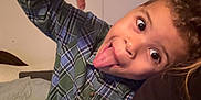 Elijah joined the competition — help win amazing prizes! child, playful, tongue_out, plaid_shirt, indoor, person, curly_hair, smile, gesture, young, casual_clothing, bedroom, fun, portrait, face, happy, cute, expression, human, silly