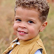 Elijah is registered to the contest to win money with this photo: child, boy, smiling, curly_hair, portrait, outdoor, vest, white_shirt, close_up, face, happy, young, cute, person, natural_light, background_blur, casual_clothing, skin, eyes, head