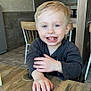 child, toddler, smiling, blond_hair, blue_eyes, indoor, table, wood, chair, casual_clothing, happy, person, face, hand, cafe, background, furniture, light, portrait, cute