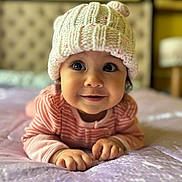 Aliah joined the competition — help win amazing prizes! baby, child, infant, knitted_hat, pink_clothing, bed, bedspread, smile, face, eyes, cute, indoors, portrait, soft_focus, warm_colors, hands, crawling, headwear, cozy, toddler
