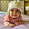 baby, child, infant, knitted_hat, pink_clothing, bed, bedspread, smile, face, eyes, cute, indoors, portrait, soft_focus, warm_colors, hands, crawling, headwear, cozy, toddler