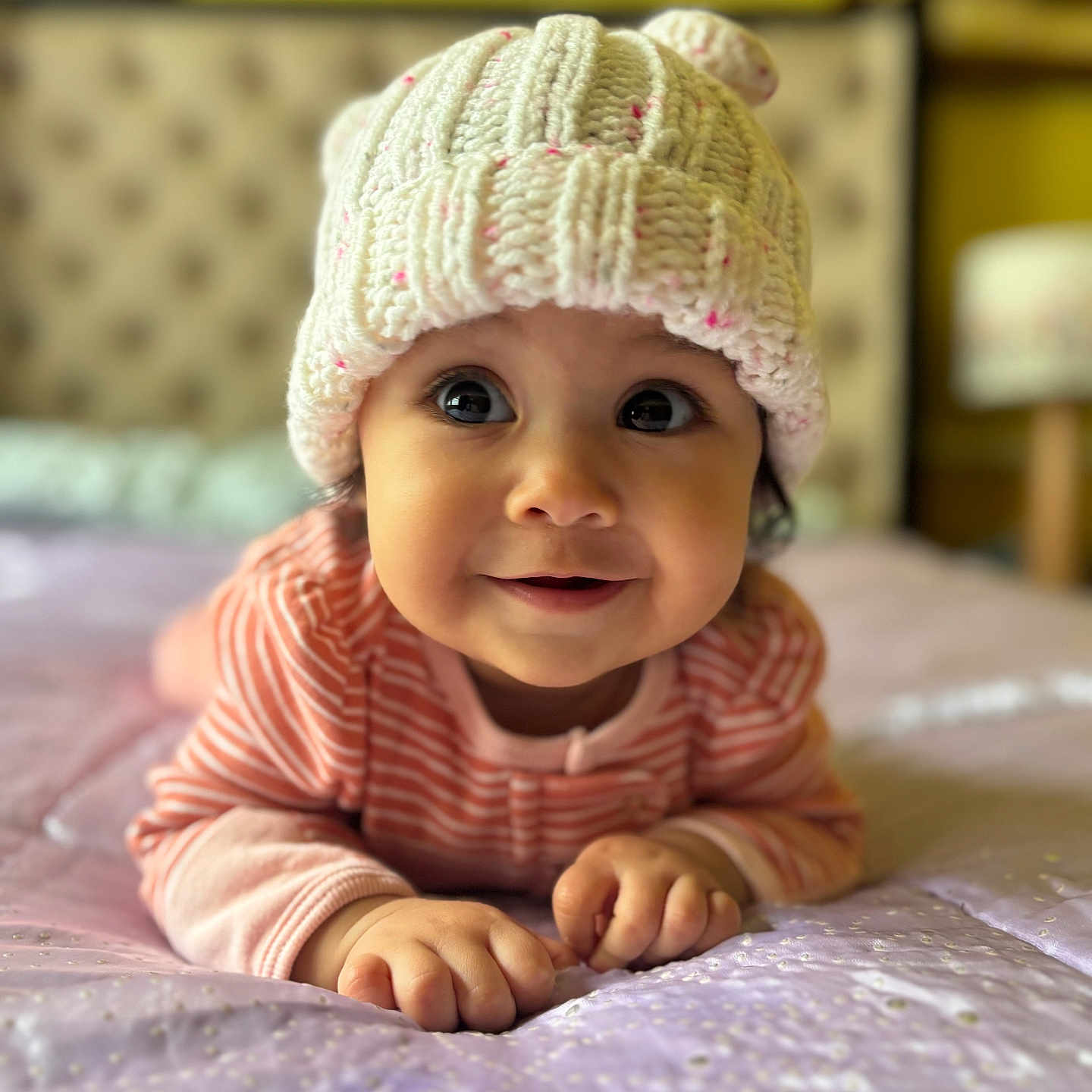 Aliah joined the competition — help win amazing prizes! baby, child, infant, knitted_hat, pink_clothing, bed, bedspread, smile, face, eyes, cute, indoors, portrait, soft_focus, warm_colors, hands, crawling, headwear, cozy, toddler