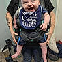 Micah joined the competition — help win amazing prizes! baby, bib, smiling, baby_carrier, tattoos, adult, vacuum_cleaner, indoor, carpet, clothing, hands, person, happy, face, legs, foot, shorts, room, home, holding