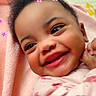 baby, smiling, face, child, pink_blanket, flower_stickers, happy, cute, infant, portrait, closeup, skin, hand, clothing, indoors, young_child, expression, soft_texture, warm_colors, joy