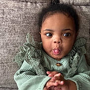 Chloe is registered to the contest to win money with this photo: toddler, child, baby, face, tongue, hands, green_clothing, lace, couch, texture, indoor, cute, expression, portrait, person, sitting, playful, curious, cozy, young_child