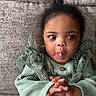 toddler, child, baby, face, tongue, hands, green_clothing, lace, couch, texture, indoor, cute, expression, portrait, person, sitting, playful, curious, cozy, young_child