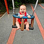 baby, child, swing, playground, smiling, happy, red_overalls, striped_shirt, outdoor, fun, joy, greenery, pavement, play, summer, park, hands, feet, blue_swing, metal_chains