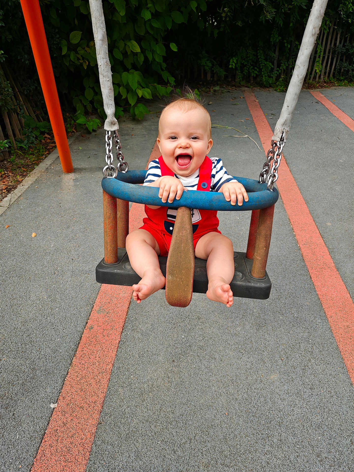 Eden participe au concours pour gagner de l'argent avec cette photo : baby, child, swing, playground, smiling, happy, red_overalls, striped_shirt, outdoor, fun, joy, greenery, pavement, play, summer, park, hands, feet, blue_swing, metal_chains