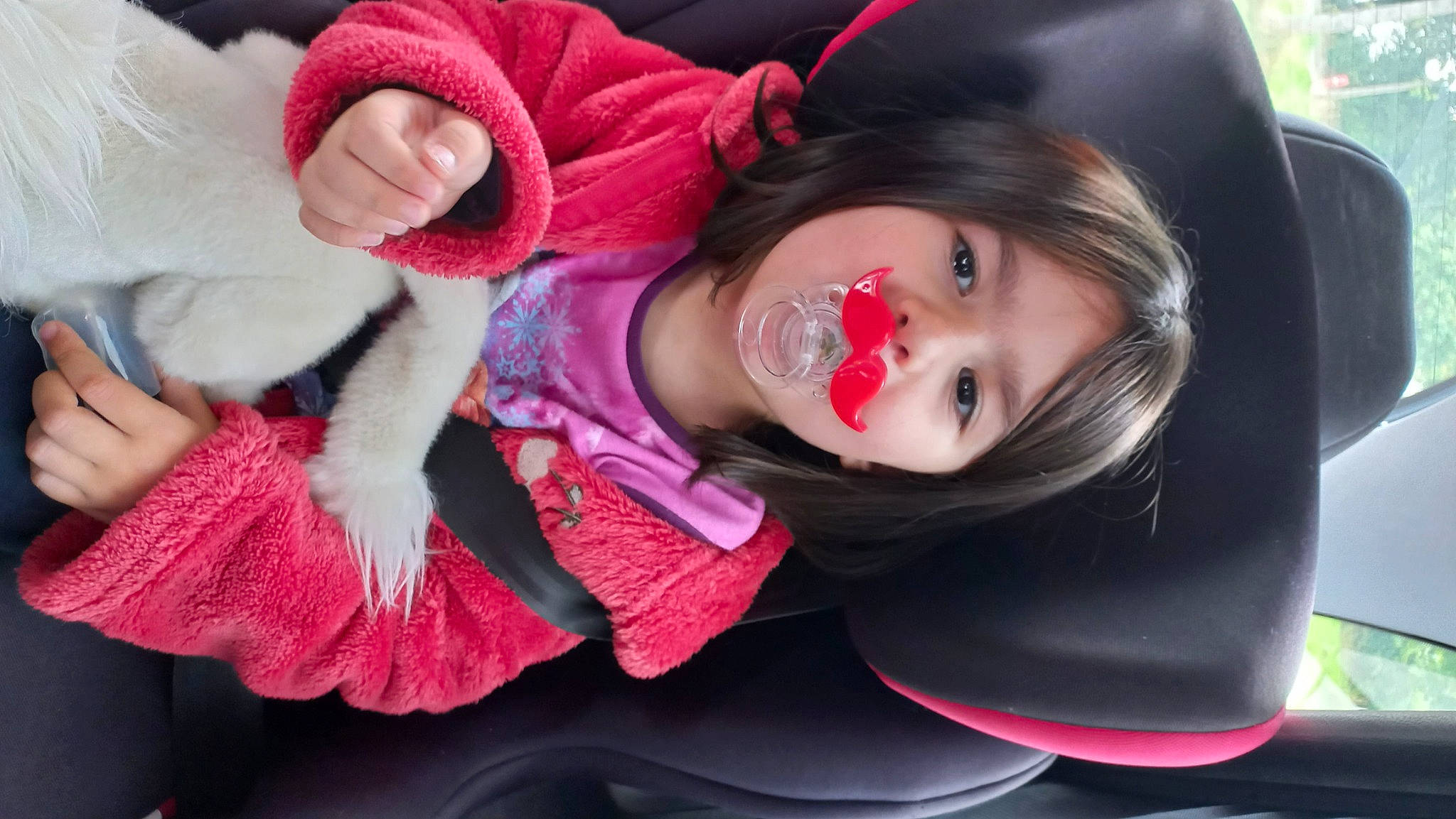 Lylou a rejoint le concours — aidez-le/la à gagner de superbes lots ! black_hair, brown_hair, child, eyebrow, eyelash, fur_clothing, grass, happy, iris, lip, long_hair, magenta, mouth, person, pink, red, sitting, skin, smile, toddler