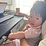 Isla is registered to the contest to win money with this photo: baby, child, infant, person, lap, pajamas, pink_clothing, desk, laptop, computer_mouse, hand, window, daylight, indoor, technology, curious, cute, adult, arm, cables
