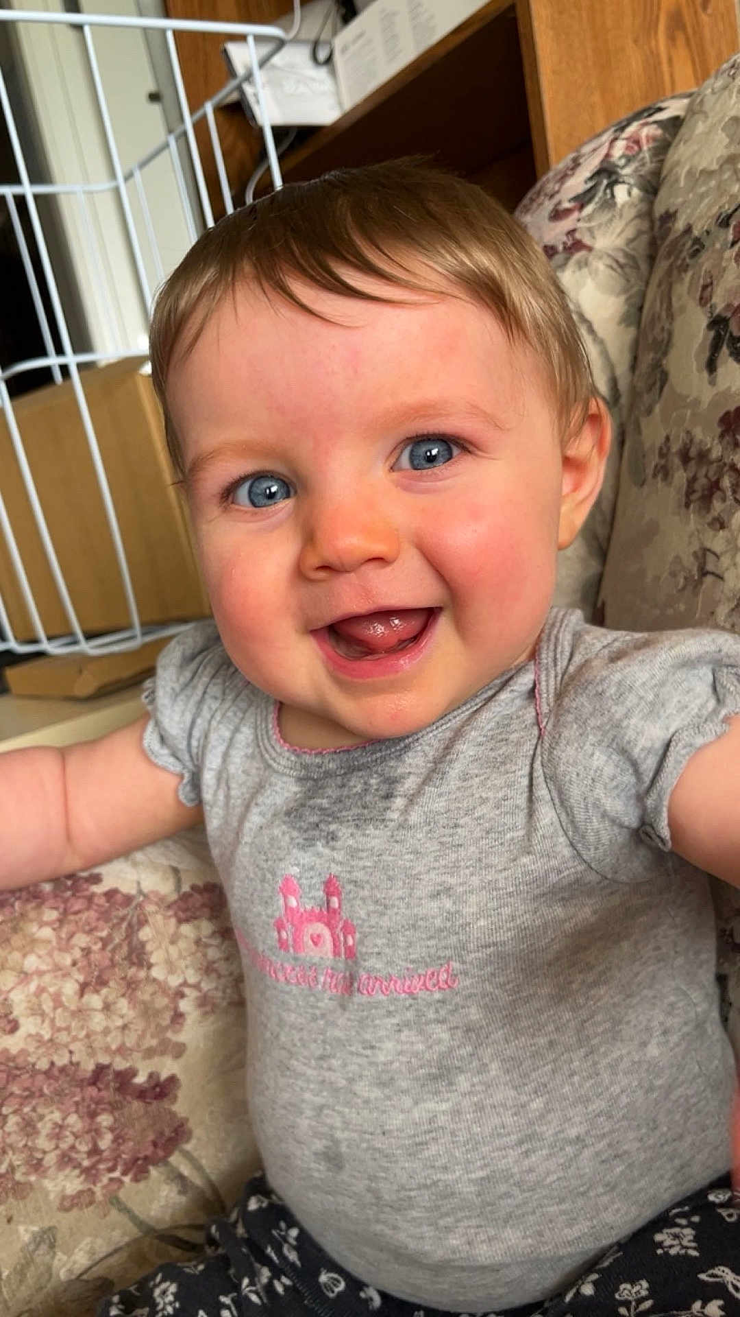 Athena joined the competition — help win amazing prizes! baby, child, smiling, blue_eyes, grey_shirt, pink_design, couch, floral_pattern, happy, indoor, person, infant, cute, portrait, sitting, short_hair, skin, face, toddler, clothing